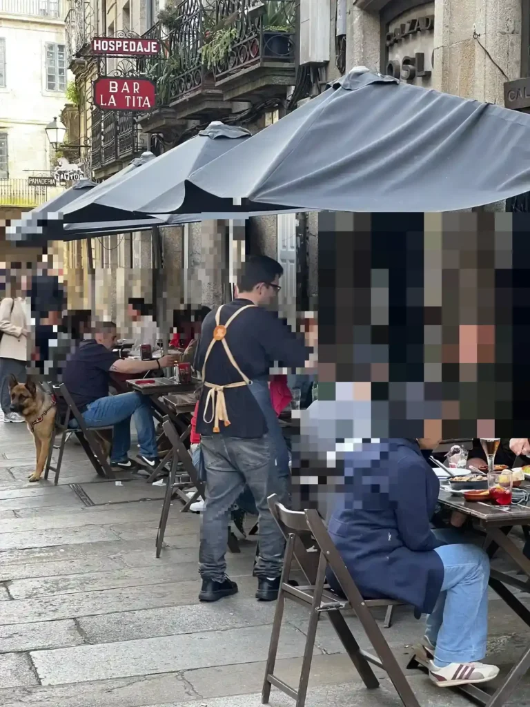 Animada terraza del Bar La Tita en el casco histórico de Santiago de Compostela, con clientes y camarero atendiendo las mesas