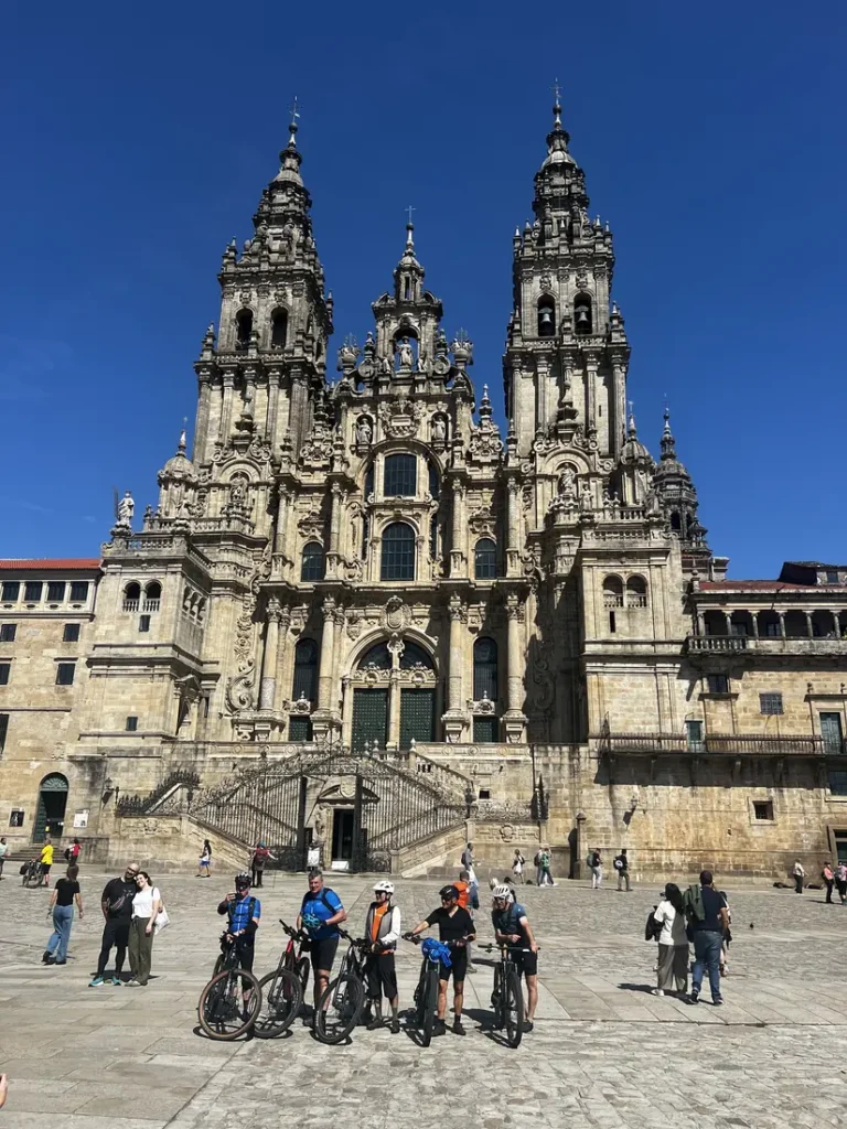 Grupo de ciclistas peregrinos posando con sus bicis frente a la fachada barroca de la Catedral de Santiago de Compostela en la Praza do Obradoiro