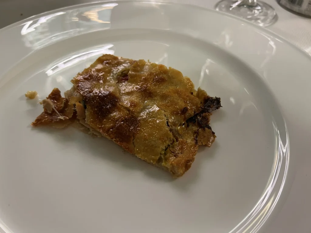 Porción de empanada gallega recién horneada con masa crujiente y dorada, servida en plato blanco en Santiago de Compostela