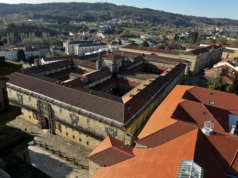 Vista aérea del Hostal de los Reyes Católicos con fachada principal a la Plaza del Obradoiro y sus cuatro claustros desde la torre de la Catedral de Santiago de Compostela, con la ciudad al fondo