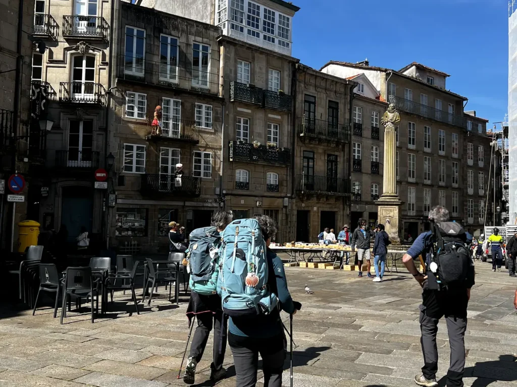 Peregrinos del Camino de Santiago cruzando la Plaza de Cervantes con sus mochilas y bastones de trekking