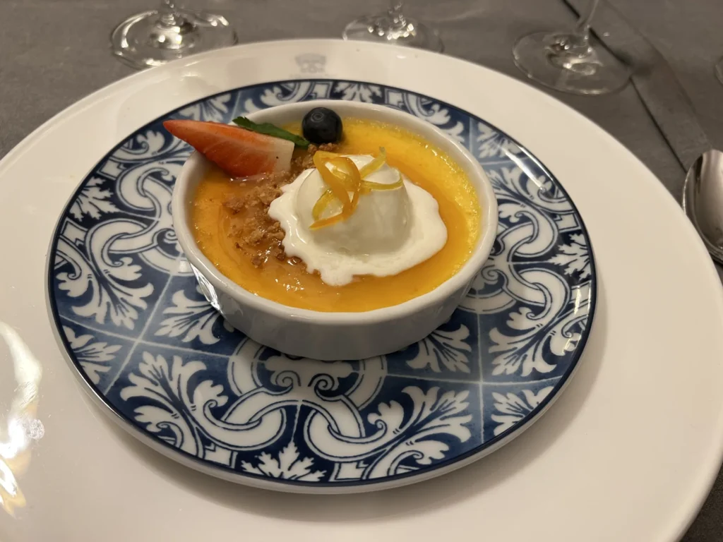 Postre de crema de limón con nata montada, crumble, fresas y arándanos servido en ramequín sobre plato de cerámica azul en el restaurante Filigrana de Santiago de Compostela
