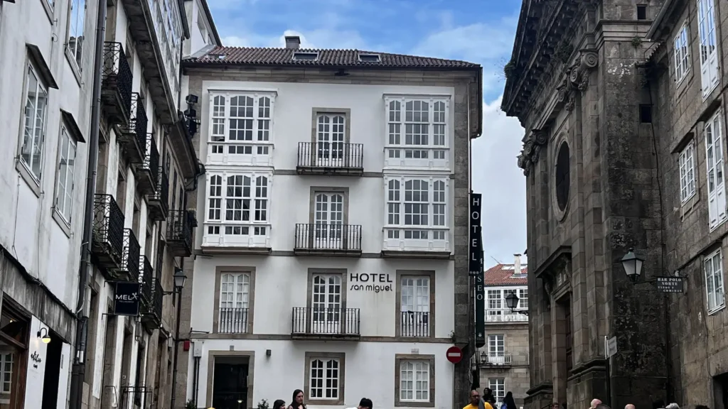 dónde alojarse en Santiago de Compostela. Plaza del casco histórico de Santiago de Compostela con el Hotel San Miguel al fondo, turistas y ambiente animado en la calle empedrada